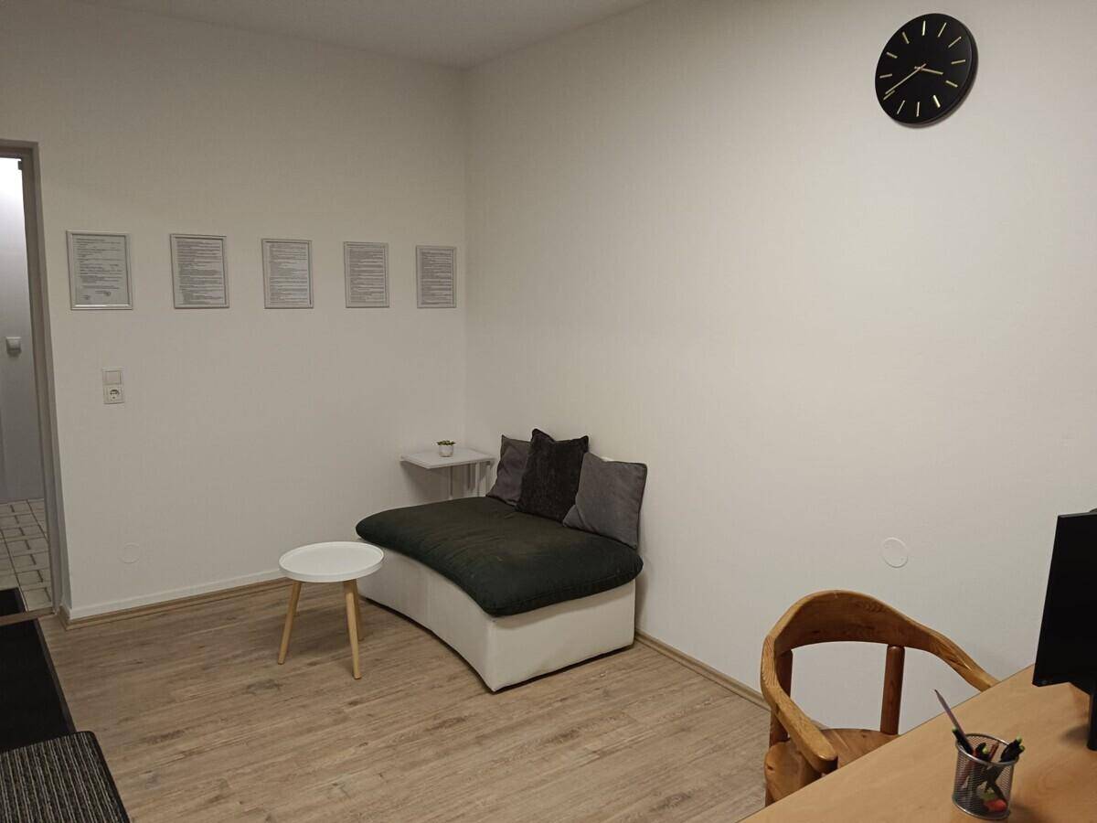 Heller Büroraum mit Schreibtisch, Sitzgelegenheit und Laminatboden.