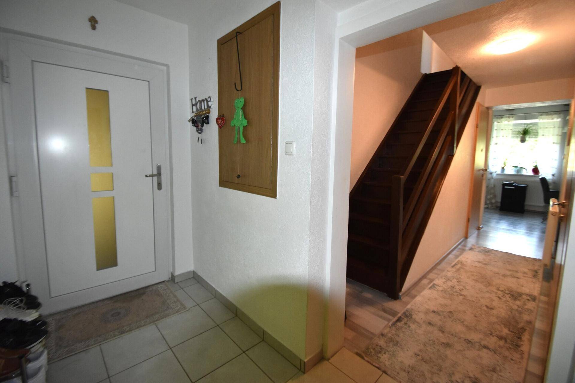 Heller Eingangsbereich mit Fliesenboden und Holztreppe zum Obergeschoss.