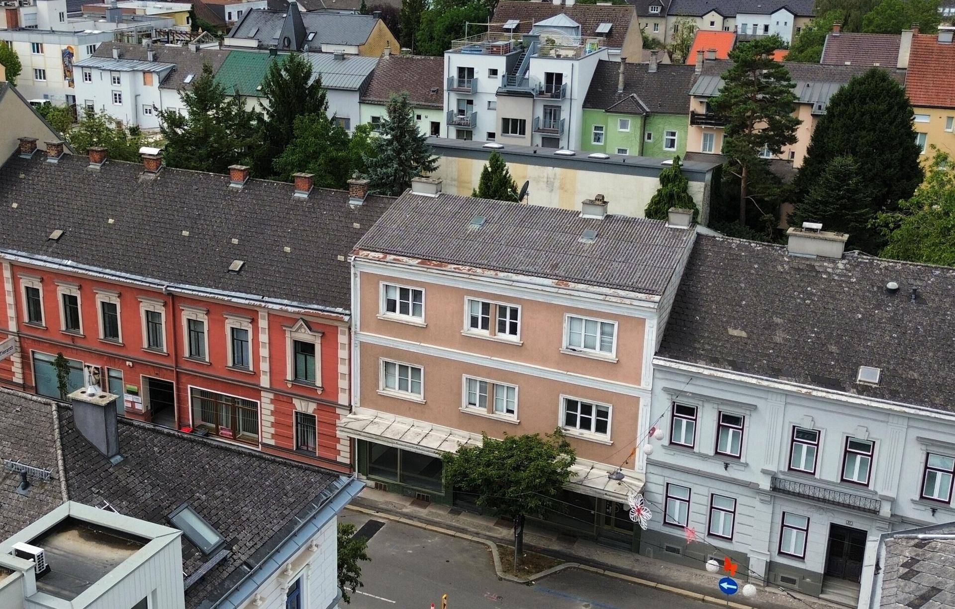 Luftaufnahme eines Gebäudes mit umliegenden Häusern und Dächern in einer städtischen Umgebung.