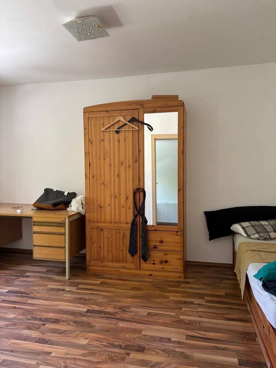 Schlafzimmer mit Holzschrank, Schreibtisch und Laminatboden, ideal für individuelle Einrichtung.
