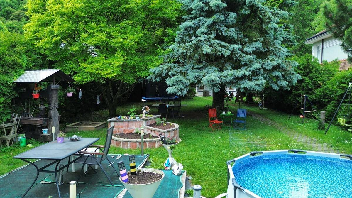 Großer Garten mit Sitzgelegenheiten, einem Aufstellpool und üppiger Vegetation.