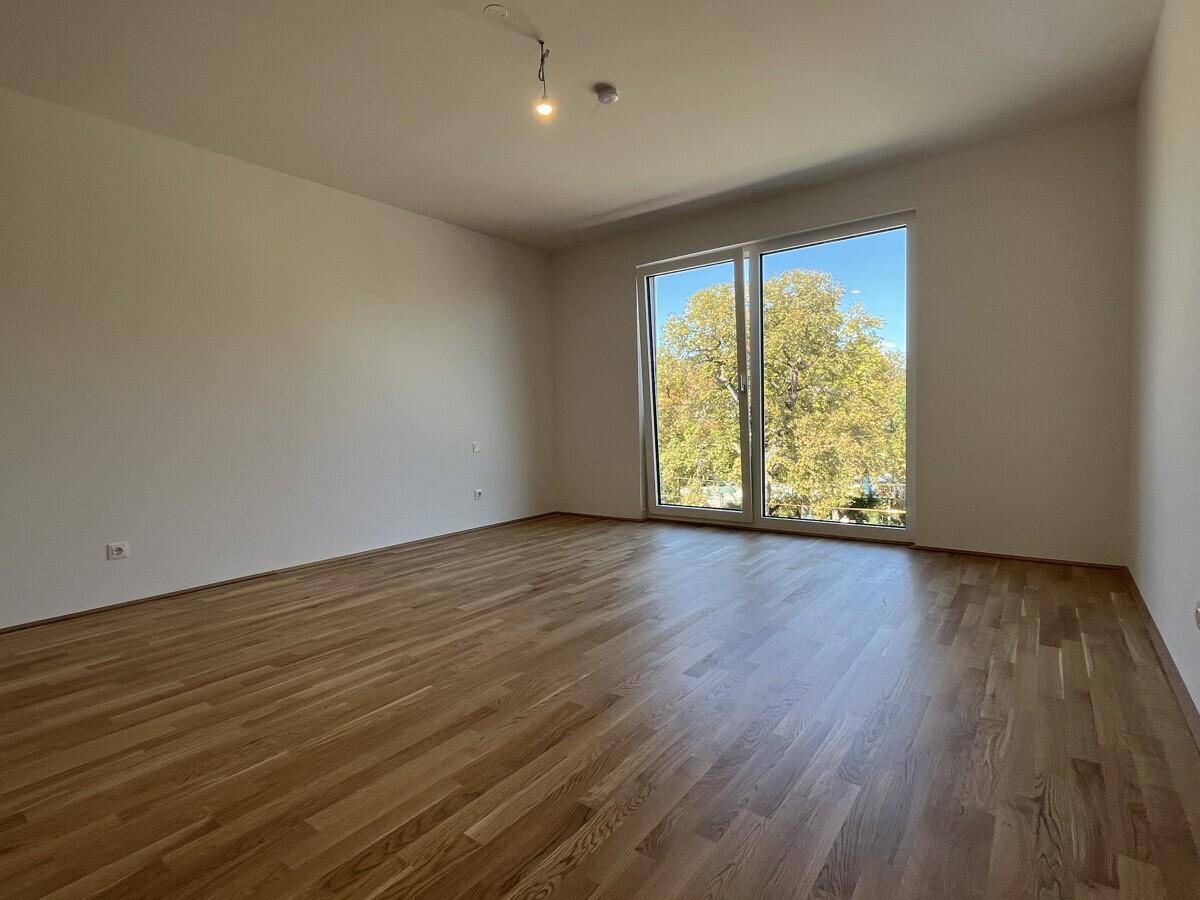 Helles Zimmer mit Parkettboden und großem Fenster, das einen grünen Ausblick bietet.