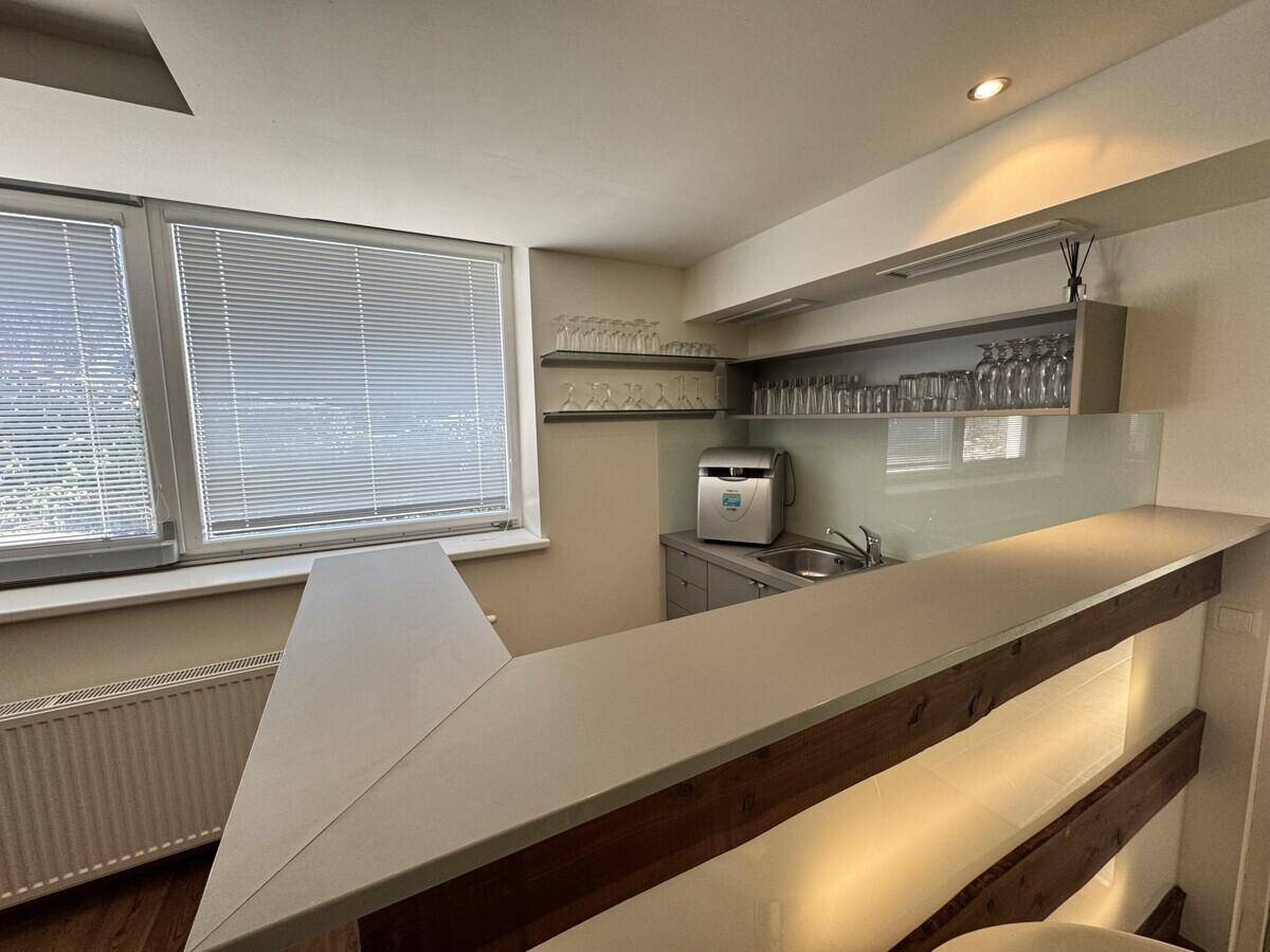 Kleine Bar mit Theke, Spüle und Regalen für Gläser, beleuchtet durch ein Fenster.