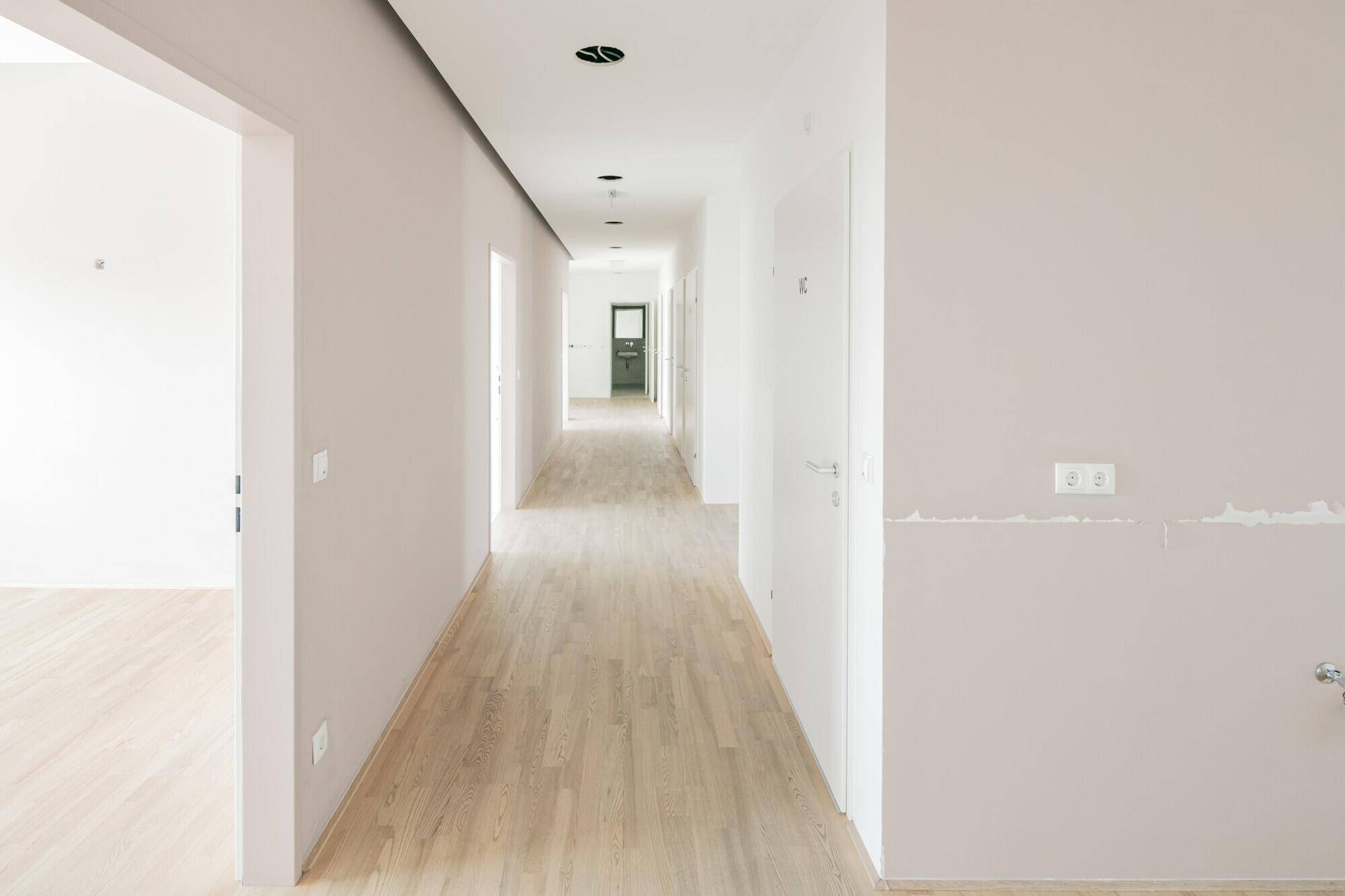 Langer, heller Flur mit Holzfußboden und mehreren Türen, der verschiedene Räume im Gebäude verbindet.