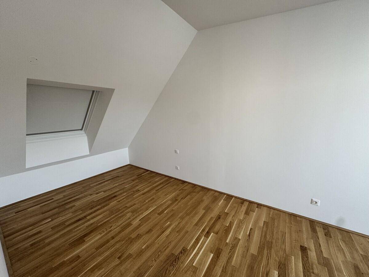 Helles Schlafzimmer im Dachgeschoss mit Holzboden und Dachfenster.