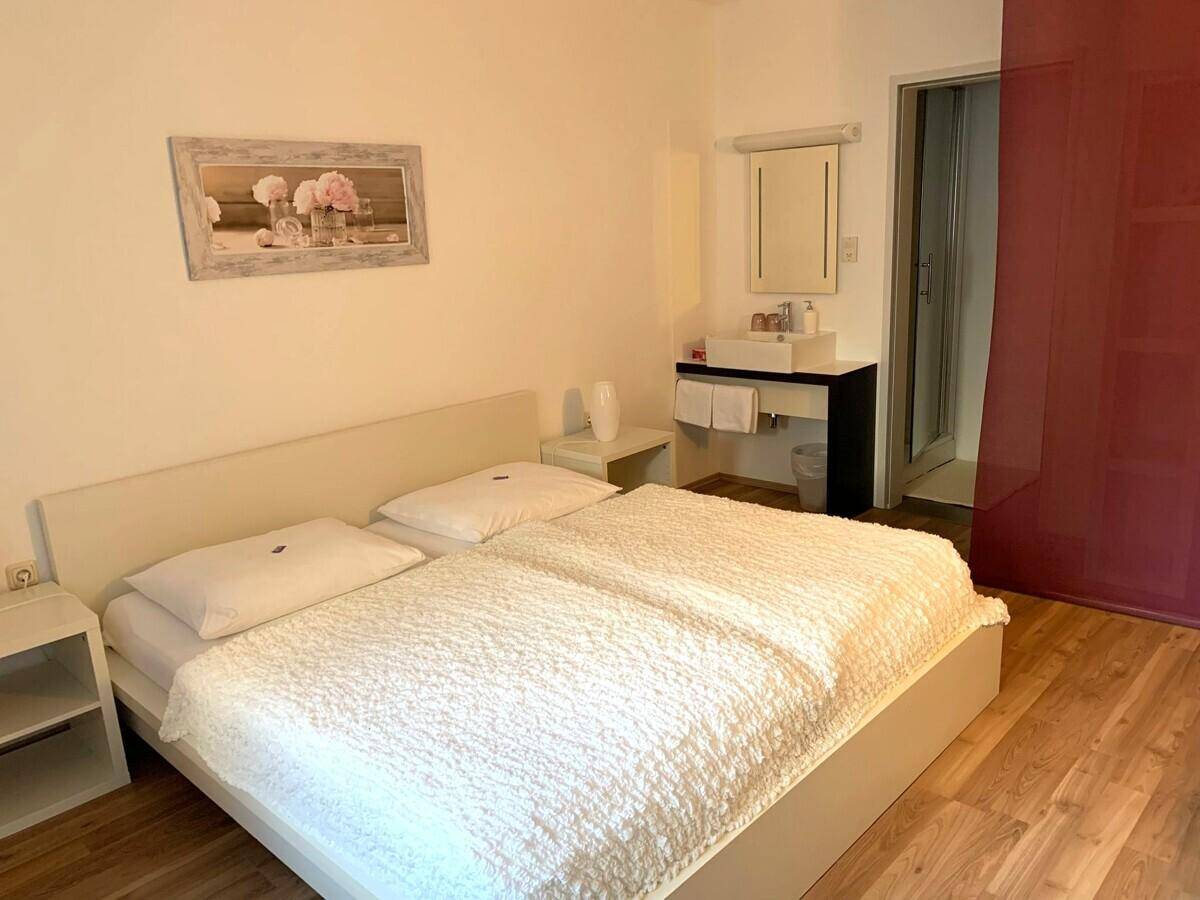 Schlafzimmer mit Doppelbett, Holzfußboden und integriertem Waschbeckenbereich.