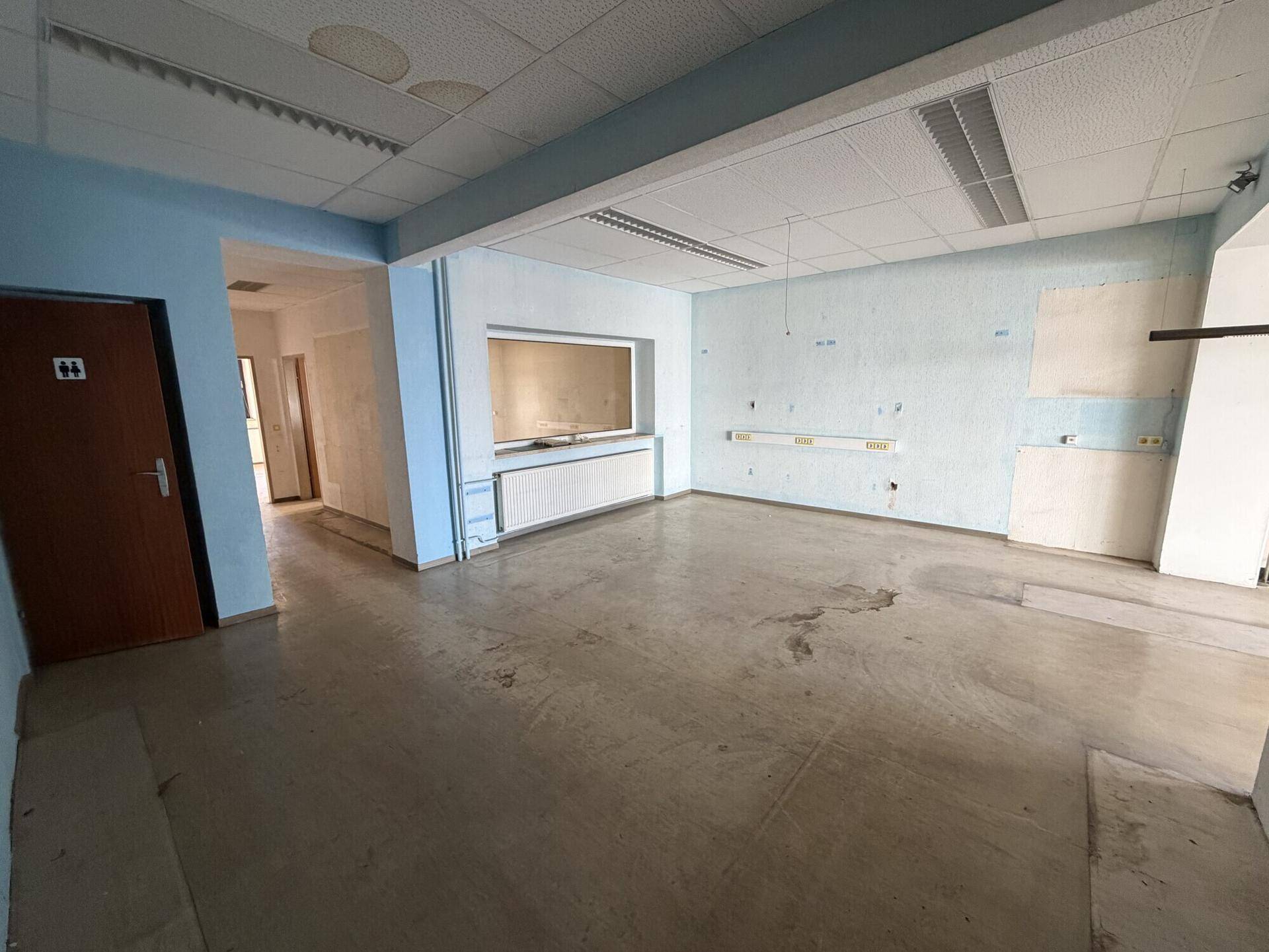 Großer, leerer Raum mit abgehängter Decke und blauen Wänden, bereit für Renovierung.