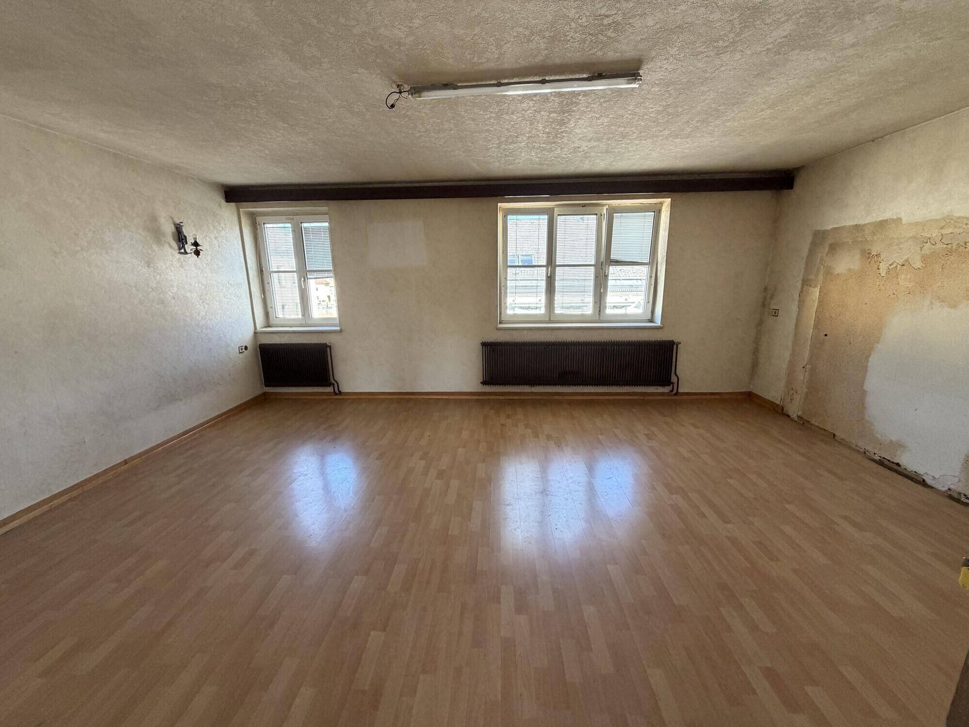 Geräumiges Wohnzimmer mit Laminatboden und zwei Fenstern, die viel Licht hereinlassen.