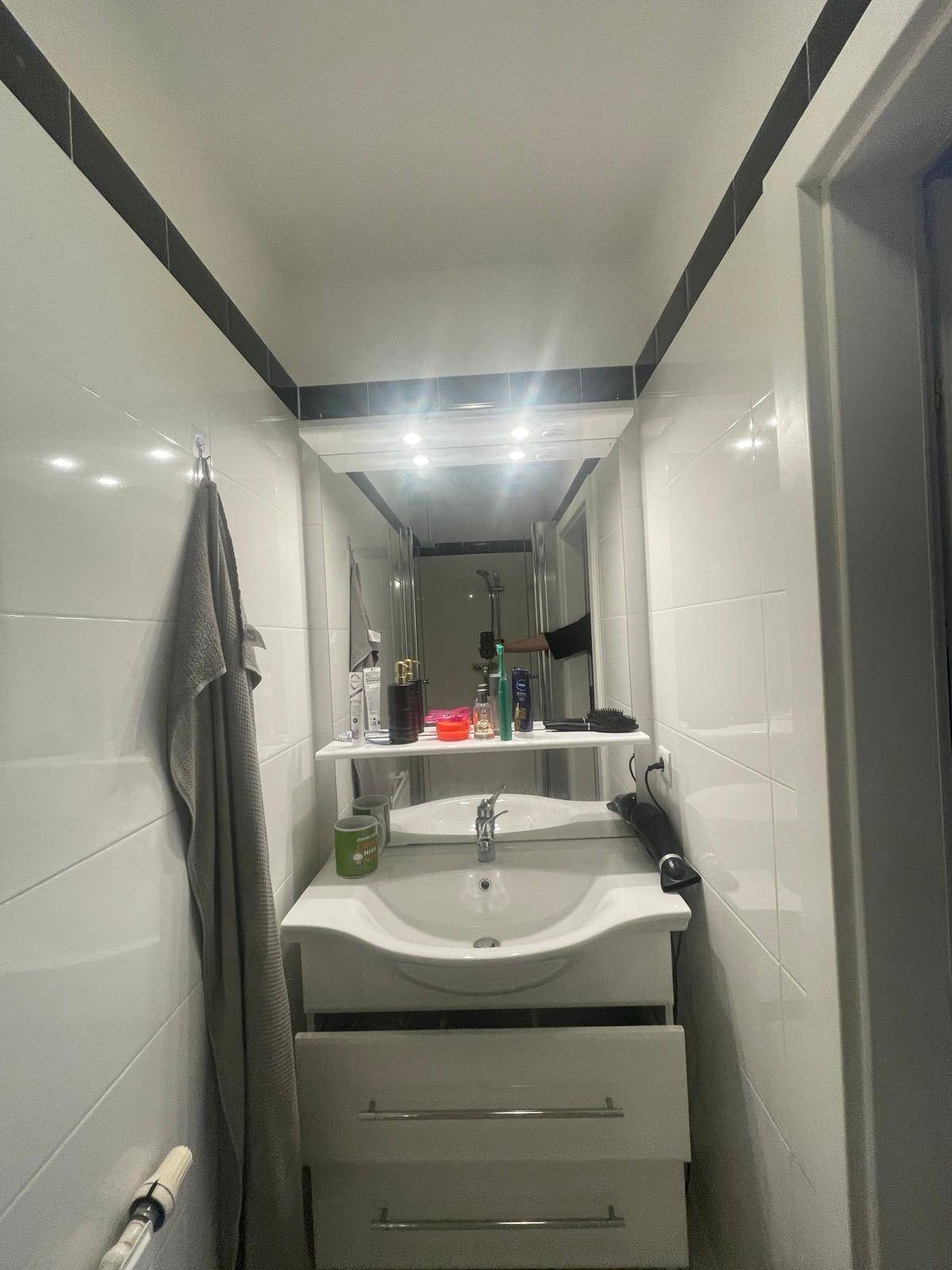 Kleines Badezimmer mit Waschbecken, Spiegel und weißen Fliesen mit schwarzem Rand.