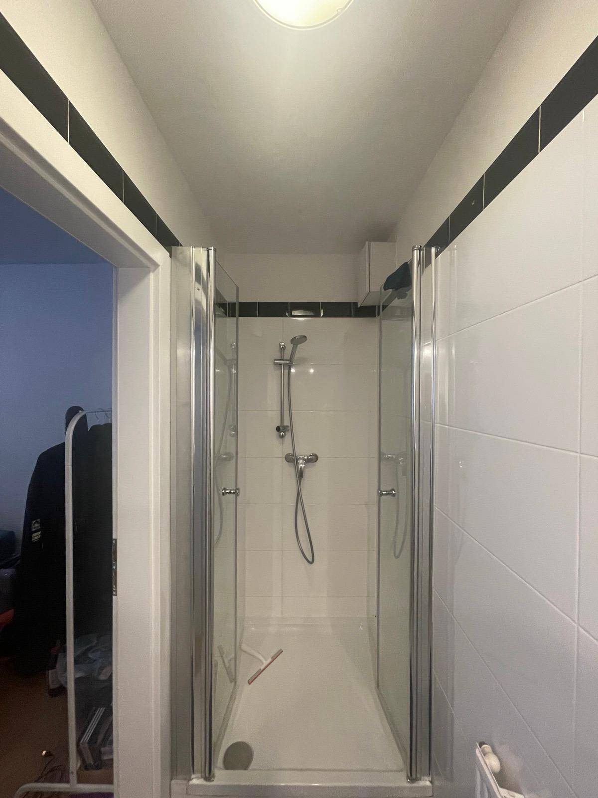 Modernes Badezimmer mit weiß gefliestem Duschbereich und schwarzem Akzentstreifen.