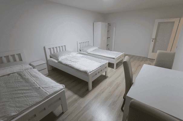 Geräumiges Schlafzimmer mit drei Einzelbetten, Schrank und hellem Laminatboden.