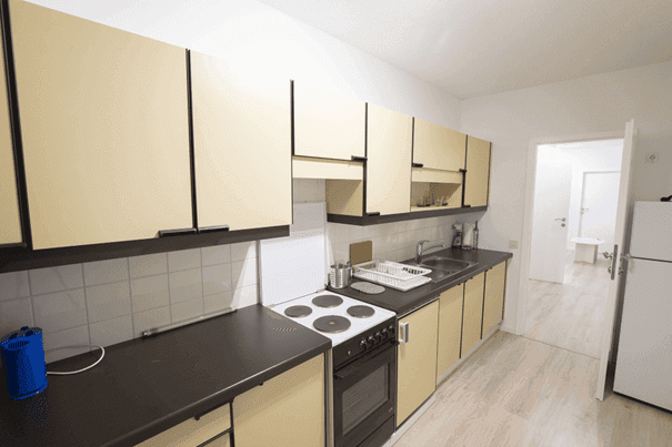 Funktionale Küche mit beigen Schränken, Elektroherd und Kühlschrank auf hellem Boden.