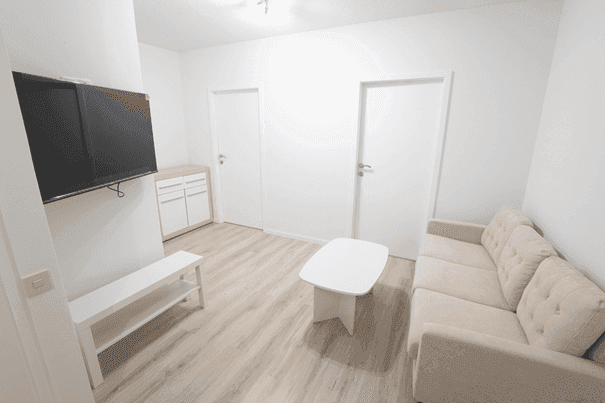 Gemütliches Wohnzimmer mit Sofa, Couchtisch und Wandfernseher auf hellem Laminatboden.