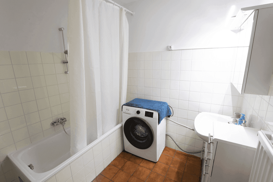 Badezimmer mit Badewanne, Waschmaschine, Waschbecken und weißen Fliesen.