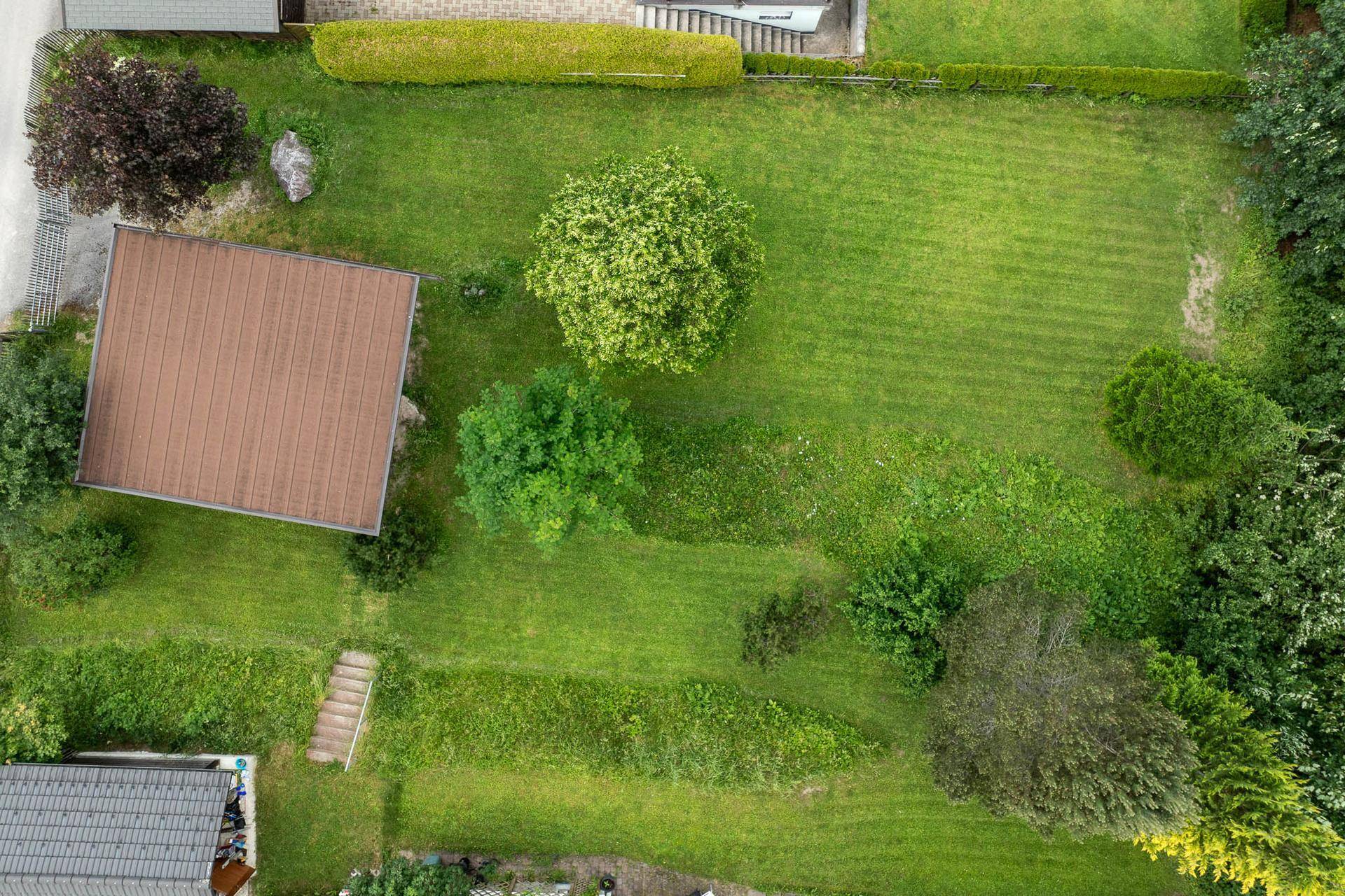 Luftaufnahme eines Grundstücks mit einem Haus, großem Garten und umliegender grüner Landschaft.