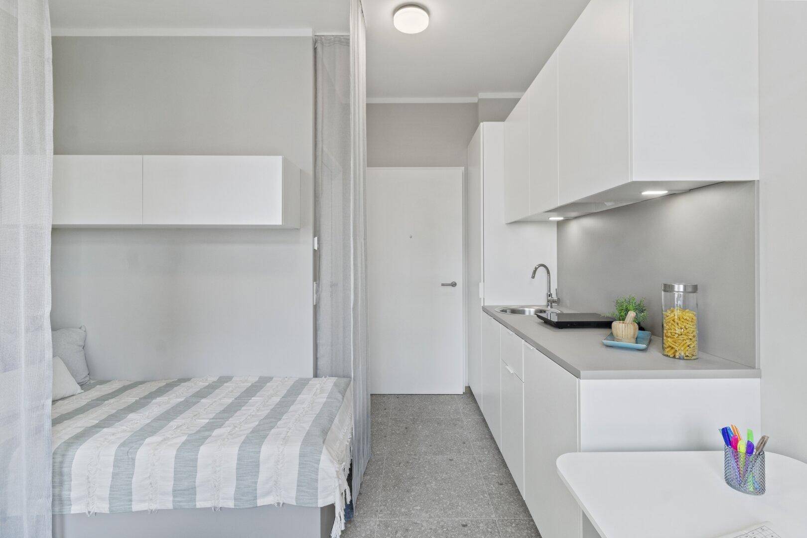 Funktionale Küchenzeile und Schlafbereich in einem modernen Studio-Apartment mit heller Einrichtung.