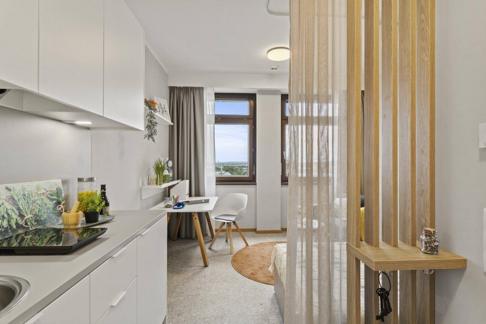 Modernes Studio-Apartment mit integrierter Küchenzeile, Schreibtisch und Blick aus dem Fenster.