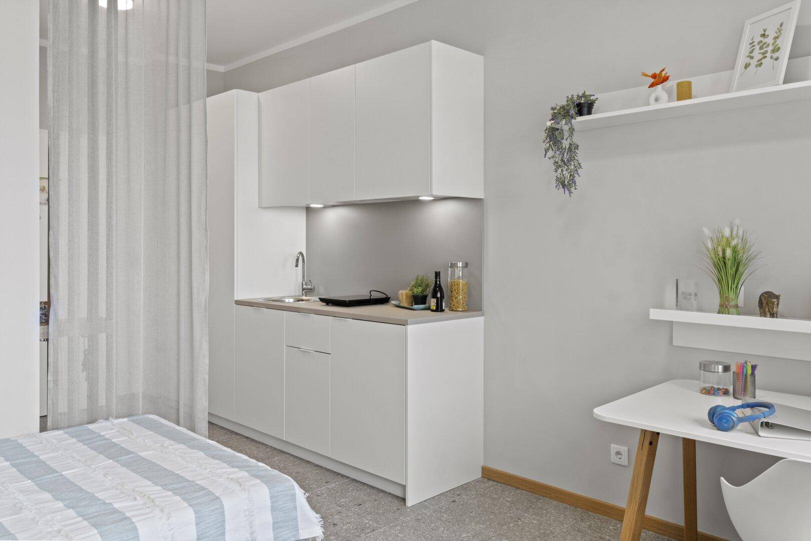 Kompakte Küchenzeile mit weißen Schränken und einem Arbeitsbereich in einem Studio-Apartment.
