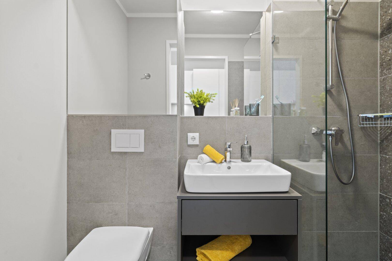 Modernes Badezimmer mit grauen Fliesen, Waschtisch und ebenerdiger Dusche.