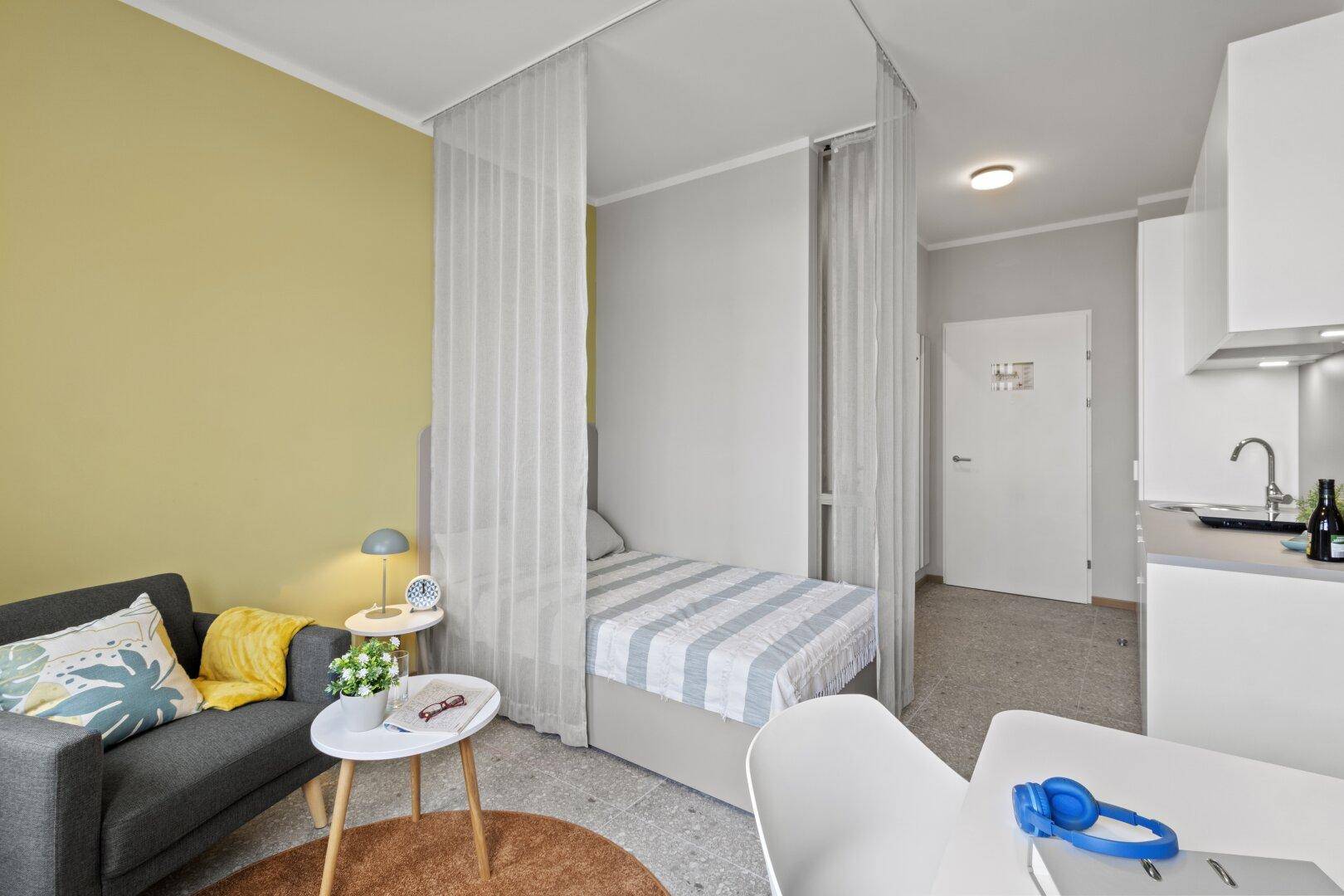 Gemütlicher Wohnbereich in einem Studio-Apartment mit Bett, Sofa und angrenzender Küchenzeile.