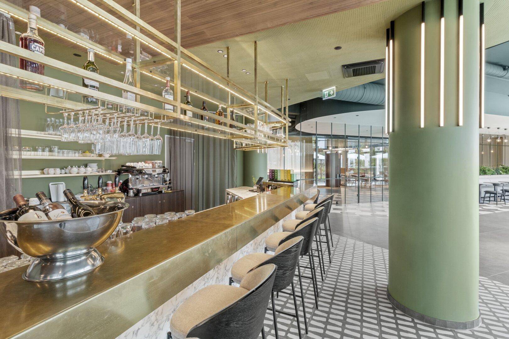 Elegante Bar mit goldener Theke, hohen Hockern und stilvoller Beleuchtung in einem Gemeinschaftsbereich.