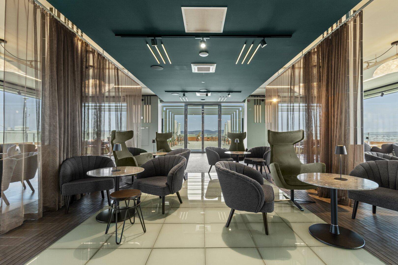 Stilvolle Lounge mit bequemen Sesseln, dunkler Decke und großen Fenstern mit Weitblick.
