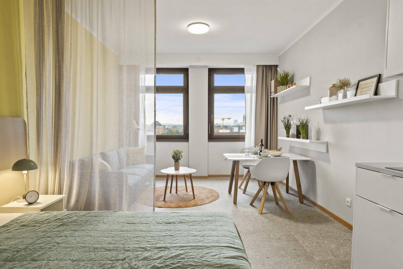 Helles Studio-Apartment mit Schlafbereich, Essplatz und Blick auf die Stadt.