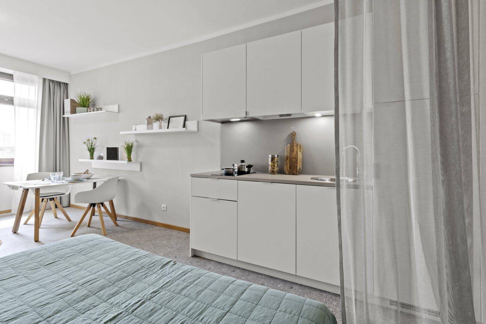 Funktionales Studio-Apartment mit Küchenzeile, Essbereich und abgetrenntem Schlafbereich.