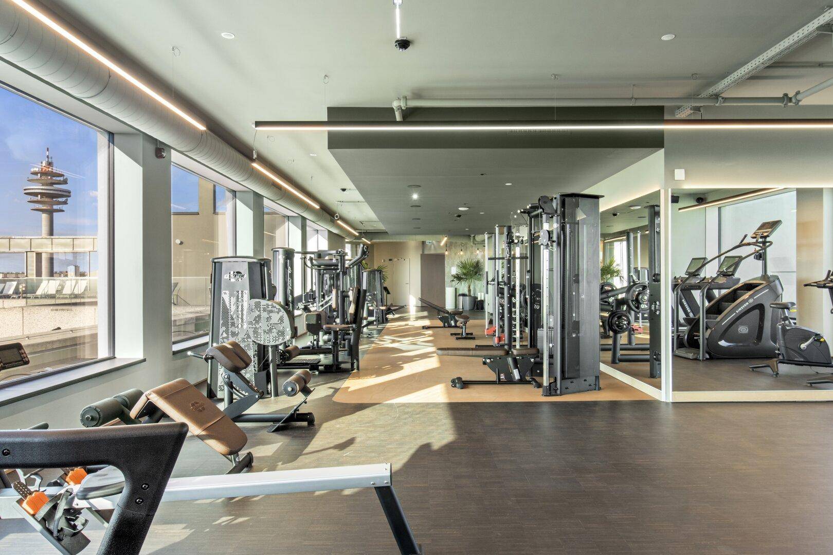 Modernes Fitnessstudio mit vielfältigen Geräten, großen Fenstern und Panoramablick auf die Stadt.