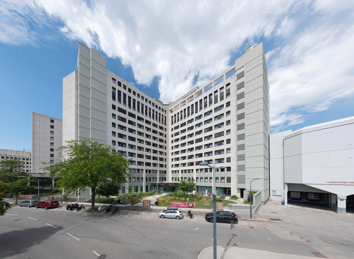Modernes Gebäude mit geschwungener Fassade und zahlreichen Fenstern unter blauem Himmel.