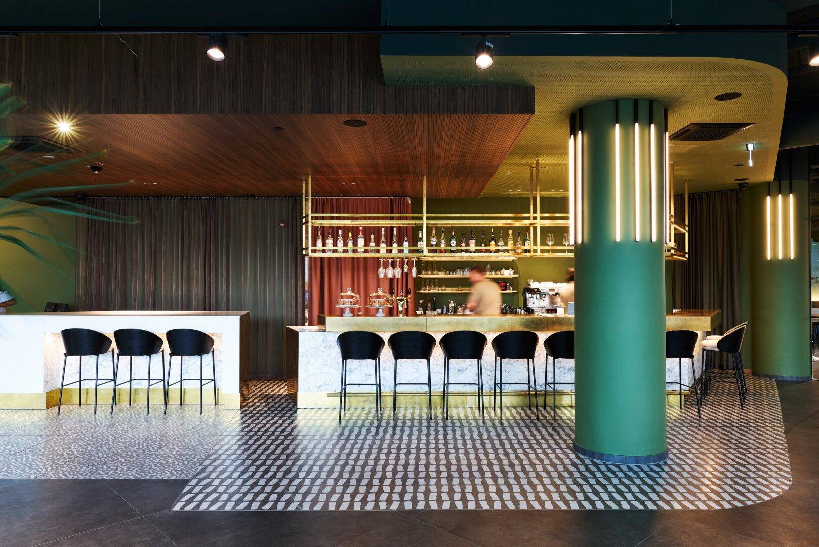 Moderne Bar mit grünen Akzenten, Holzakzenten und stilvollen Barhockern, die eine einladende Atmosphäre schaffen.