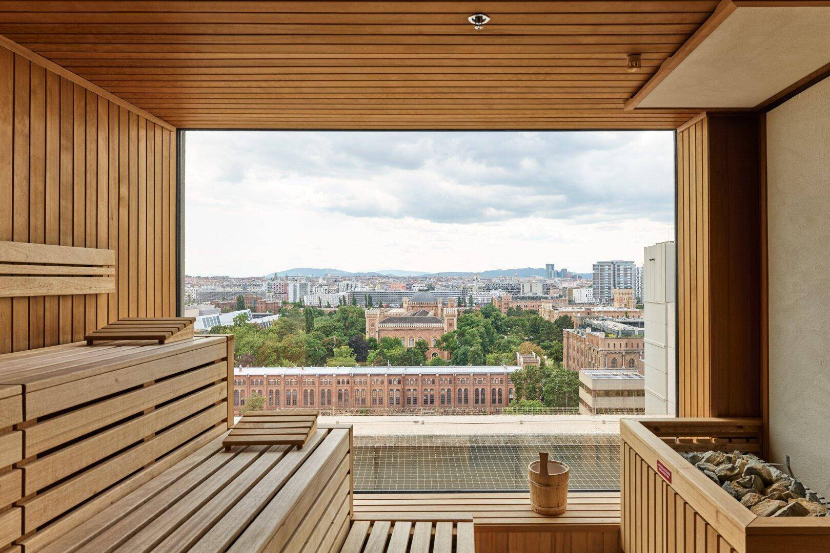 Moderne Sauna mit Holzbänken und einem großen Fenster, das einen weiten Panoramablick über die Stadt bietet.