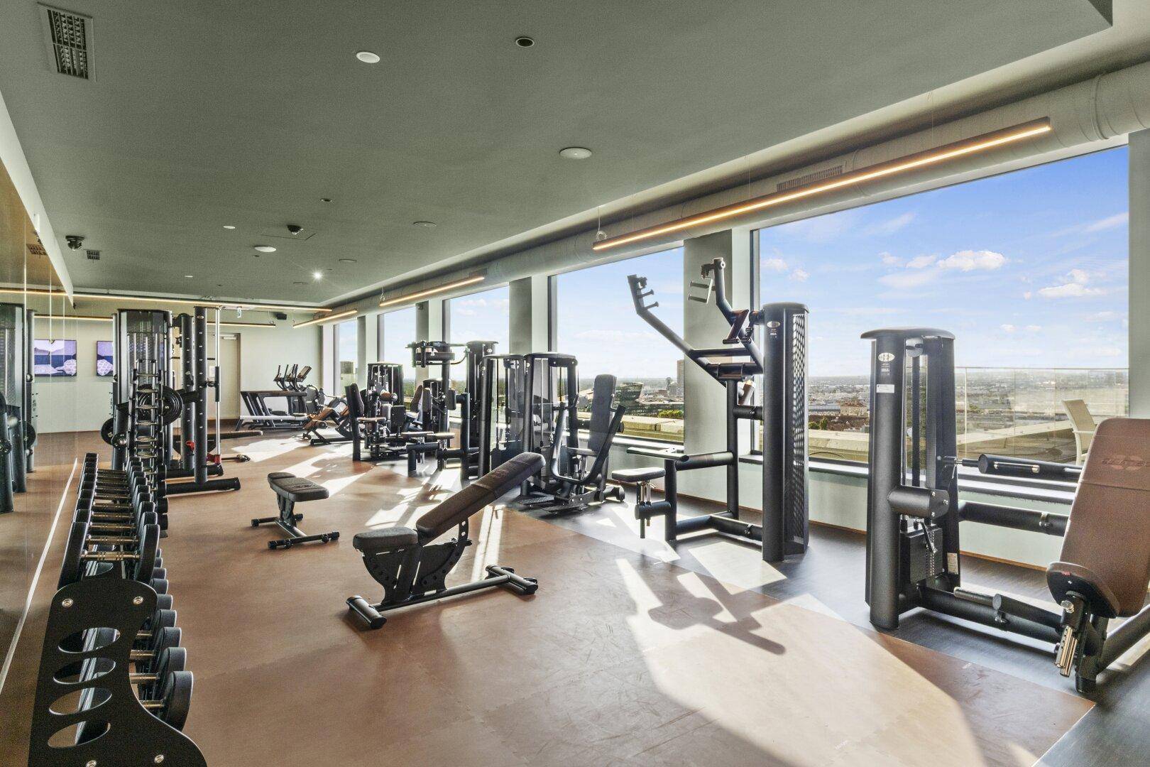 Modernes Fitnessstudio mit vielfältigen Trainingsgeräten und großen Fenstern, die einen weiten Ausblick bieten.