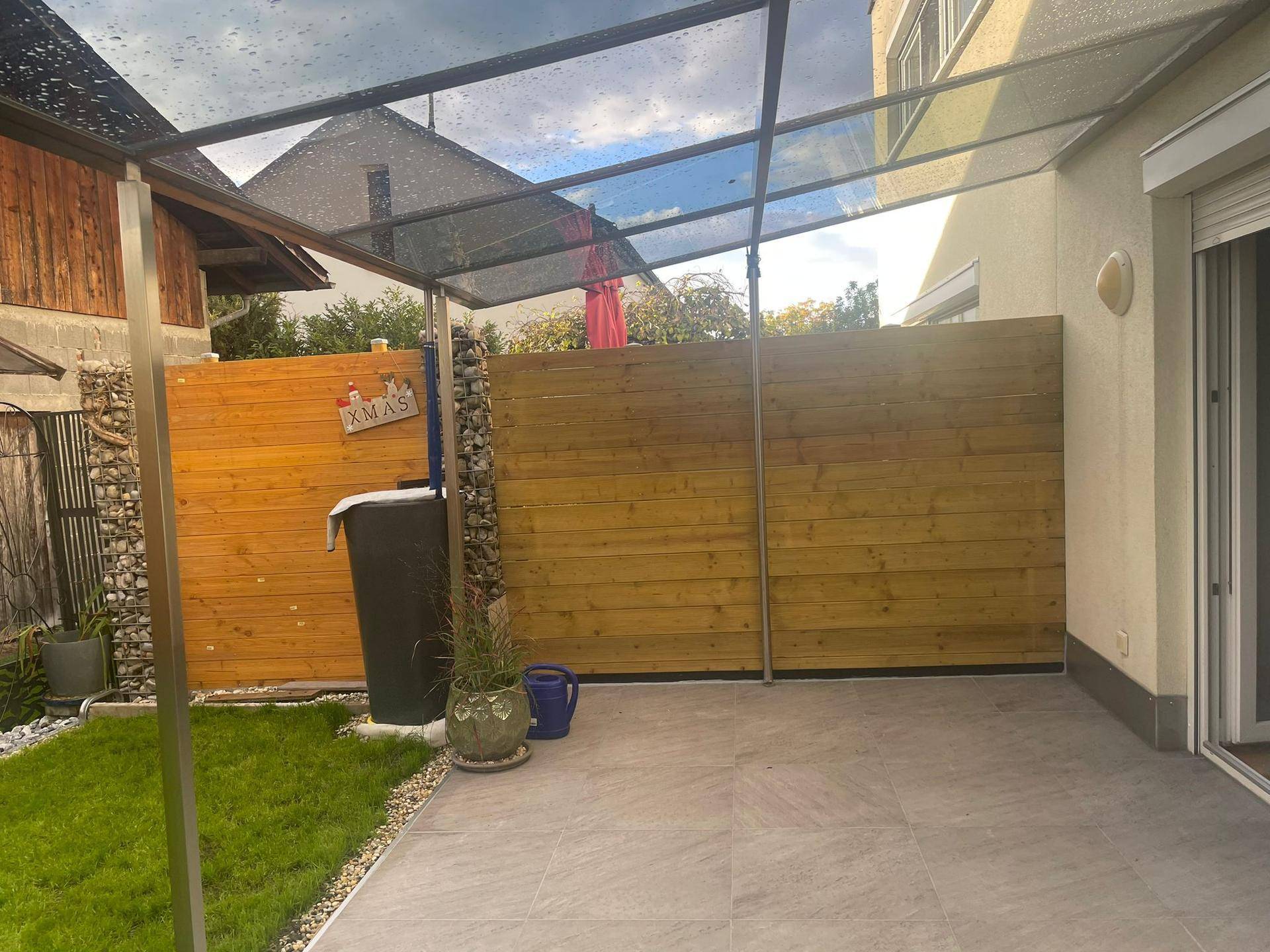 Überdachter Terrassenbereich mit Holzabtrennung und Blick in den Garten.