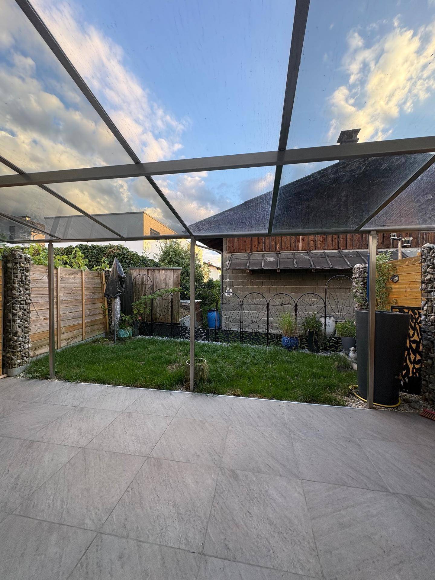 Überdachte Terrasse mit gepflastertem Bereich und kleinem Rasenstück im Garten.