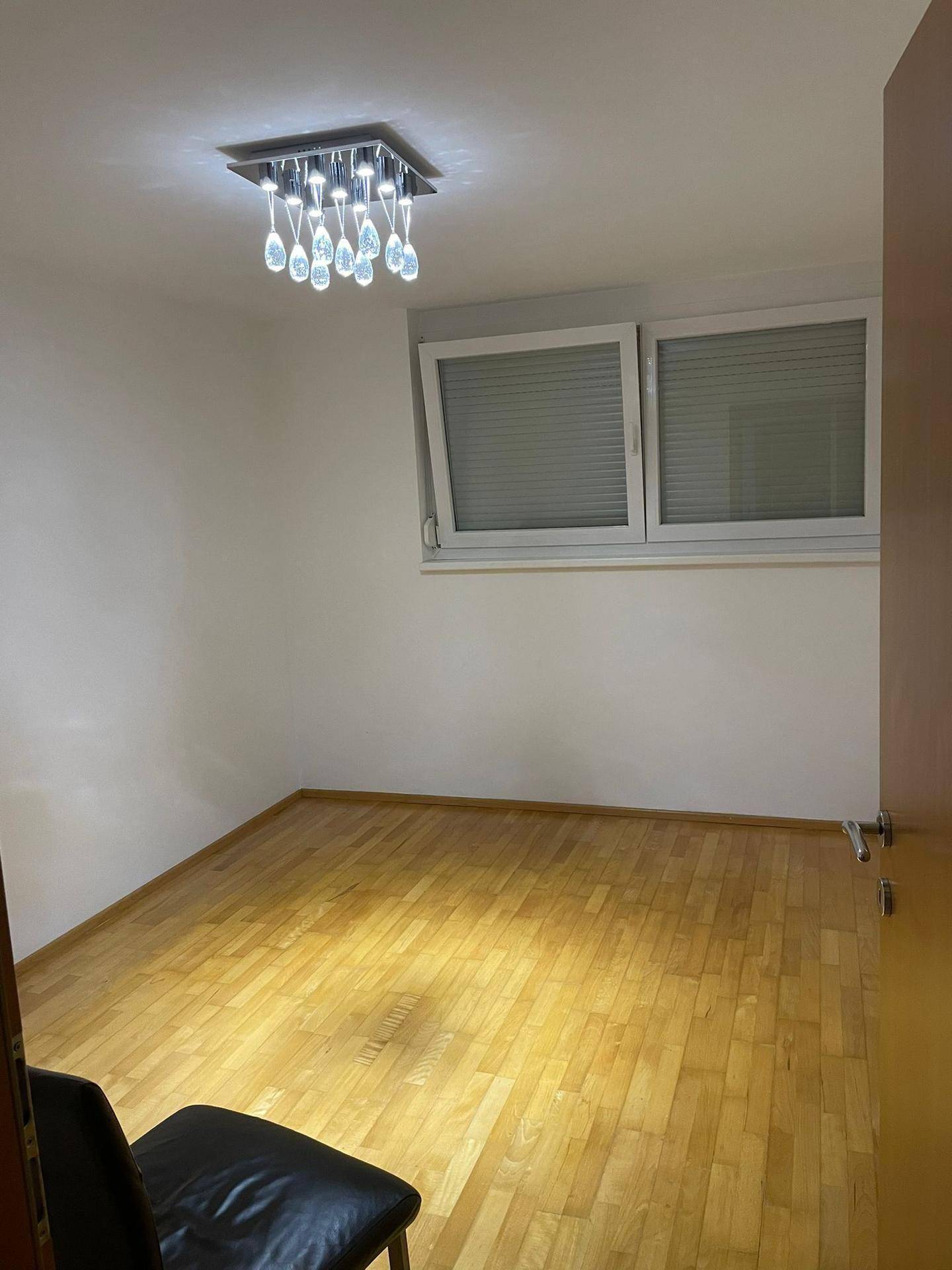 Leeres Schlafzimmer mit hellem Holzparkett und einem Fenster mit Jalousien.