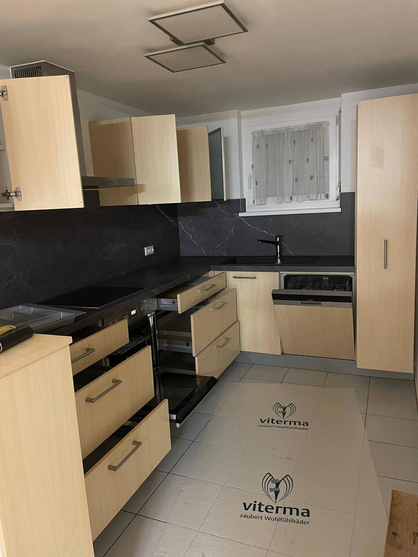 Moderne Küche mit hellen Holzschränken, dunklen Arbeitsplatten und integrierten Geräten.