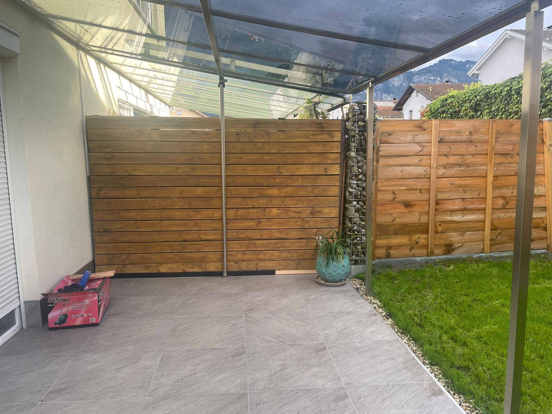 Überdachte Terrasse mit Holzabtrennung und Zugang zum Gartenbereich.