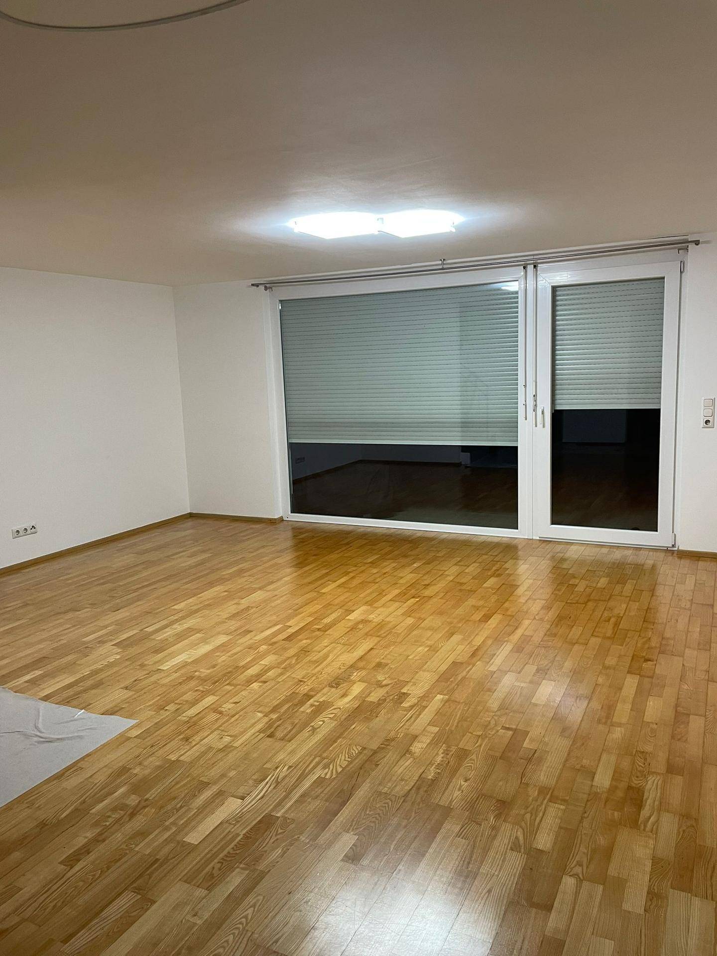 Geräumiges Wohnzimmer mit hellem Parkettboden und großen Fenstern.