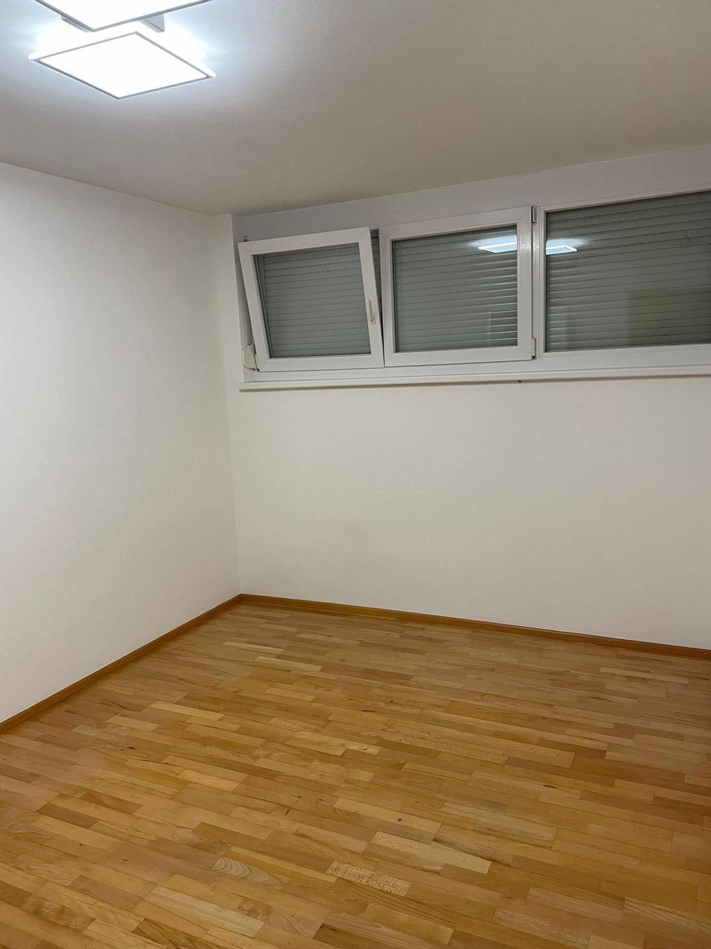 Weiteres leeres Zimmer mit Holzfußboden und Fenstern, die mit Jalousien ausgestattet sind.