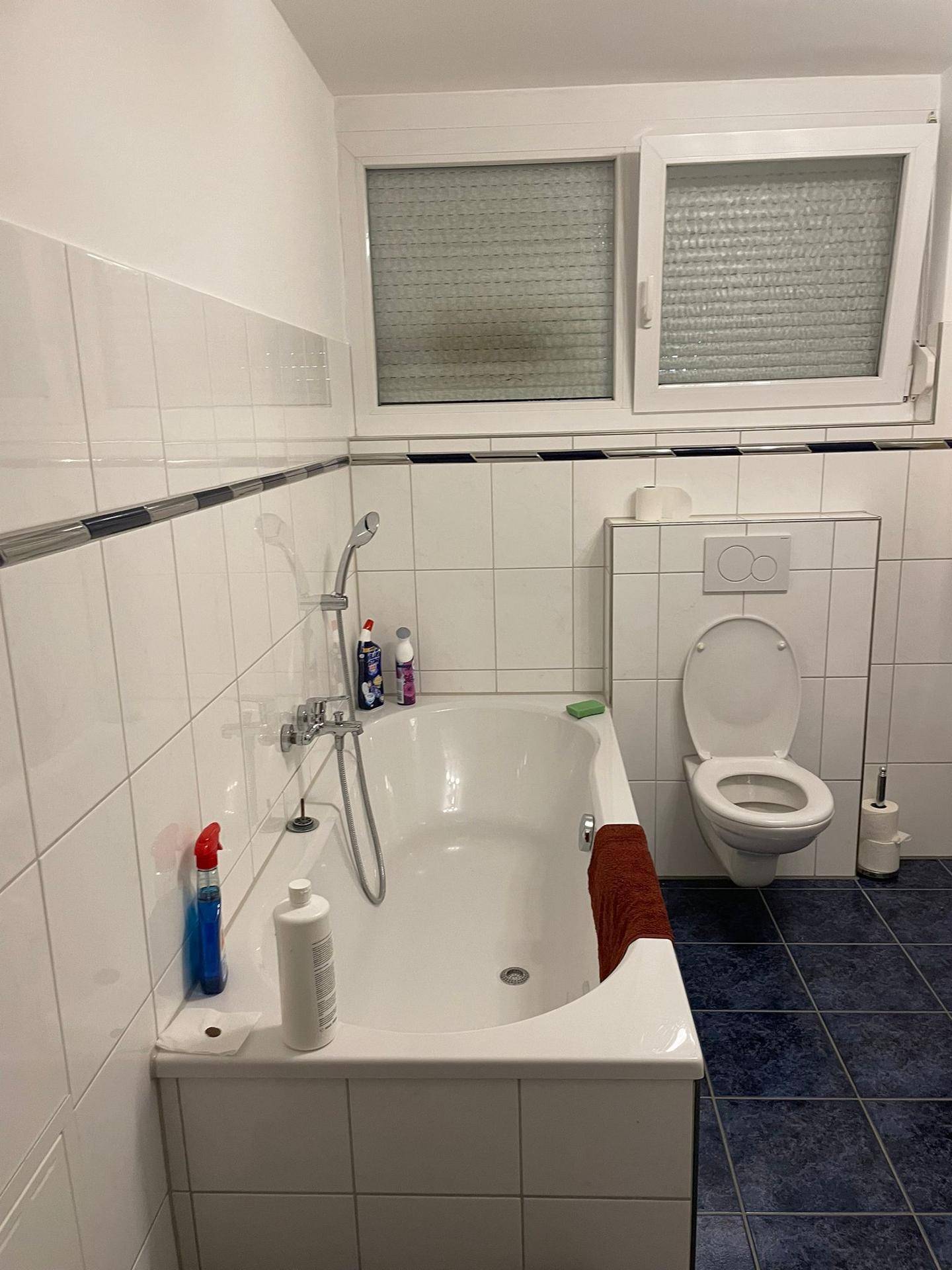 Badezimmer mit Badewanne, WC und Fenster, ausgestattet mit blauen Fliesen.