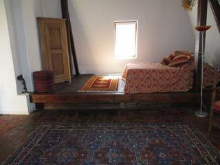 Schlafzimmer im Dachgeschoss mit Bett auf Holzpodest, Kleiderschrank und Teppich.