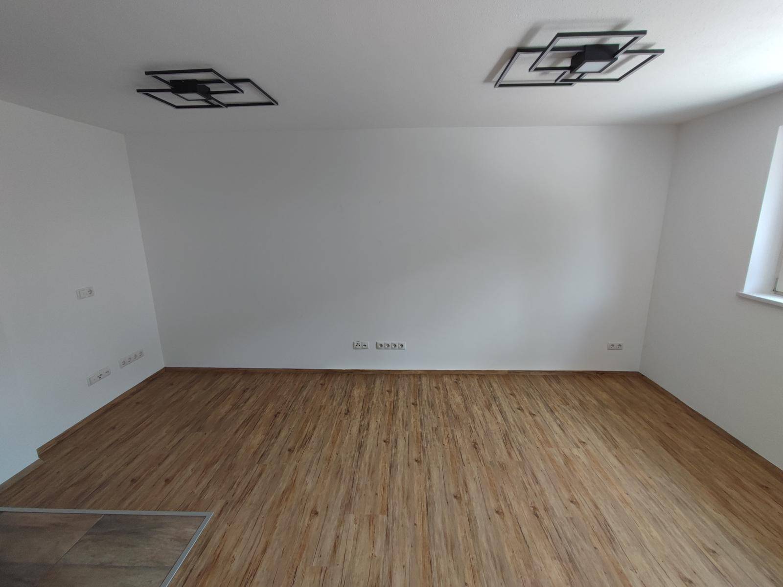 Heller, leerer Wohnraum mit Holzboden und modernen Deckenleuchten.