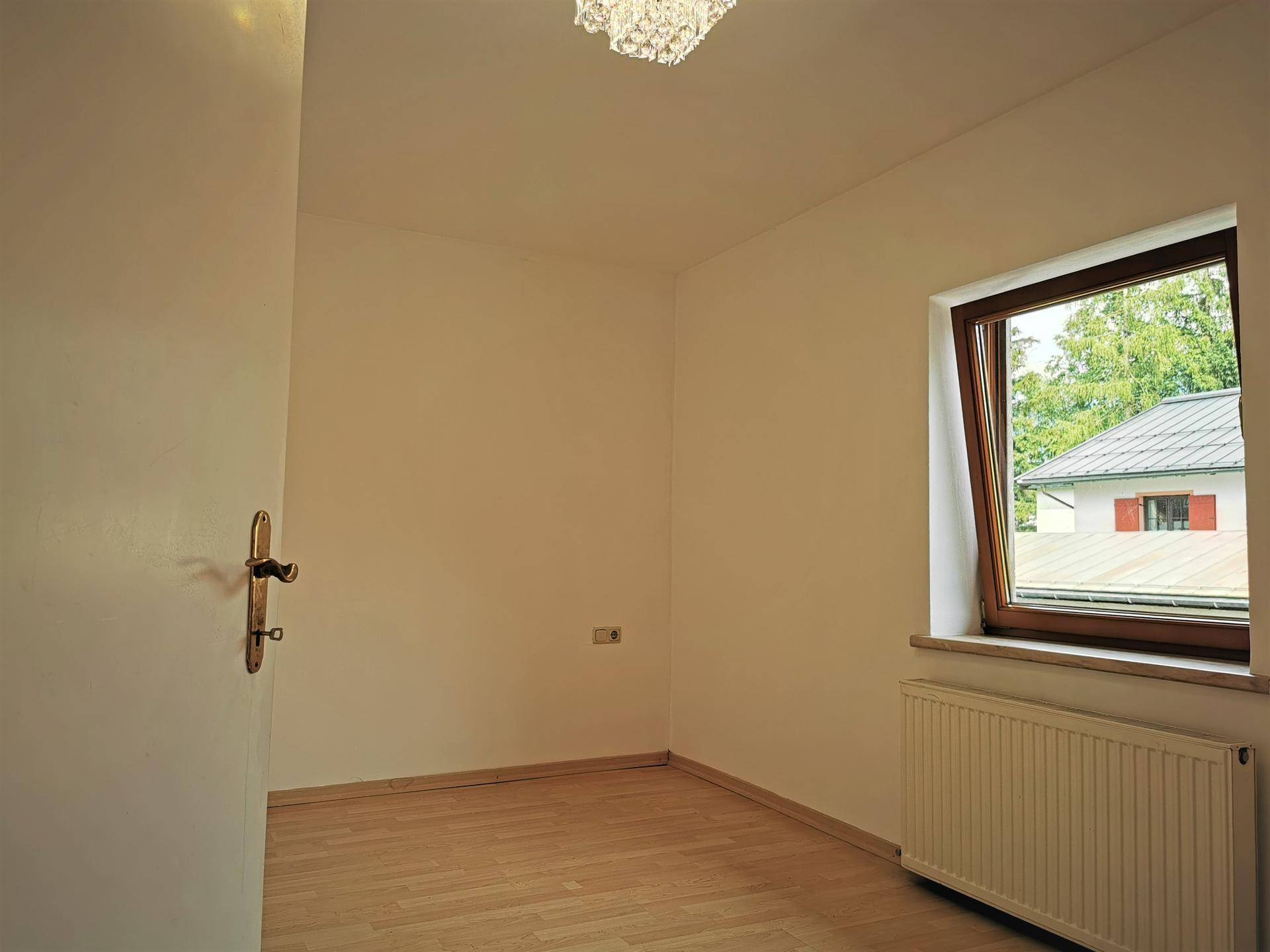 Kleiner, heller Raum mit Parkettboden und einem Fenster mit Blick auf ein Nachbarhaus, ideal als Schlafzimmer.