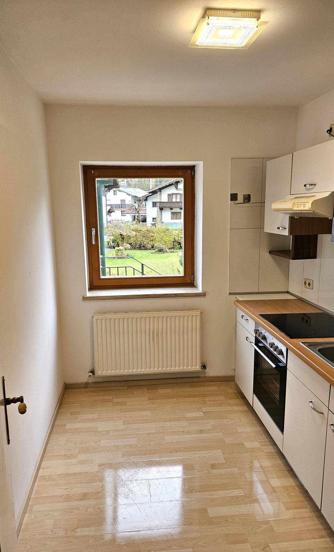 Helle Küche mit Parkettboden, Einbauküche und Fenster mit Ausblick ins Grüne, einladend und praktisch.