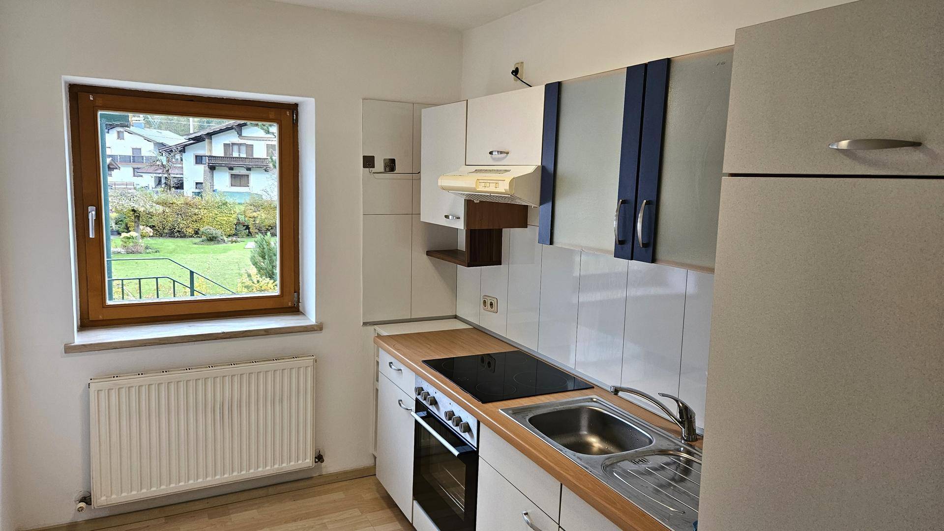 Funktionale Küche mit weißen Schränken, Holzarbeitsplatte und Blick in den Garten durch das Fenster.