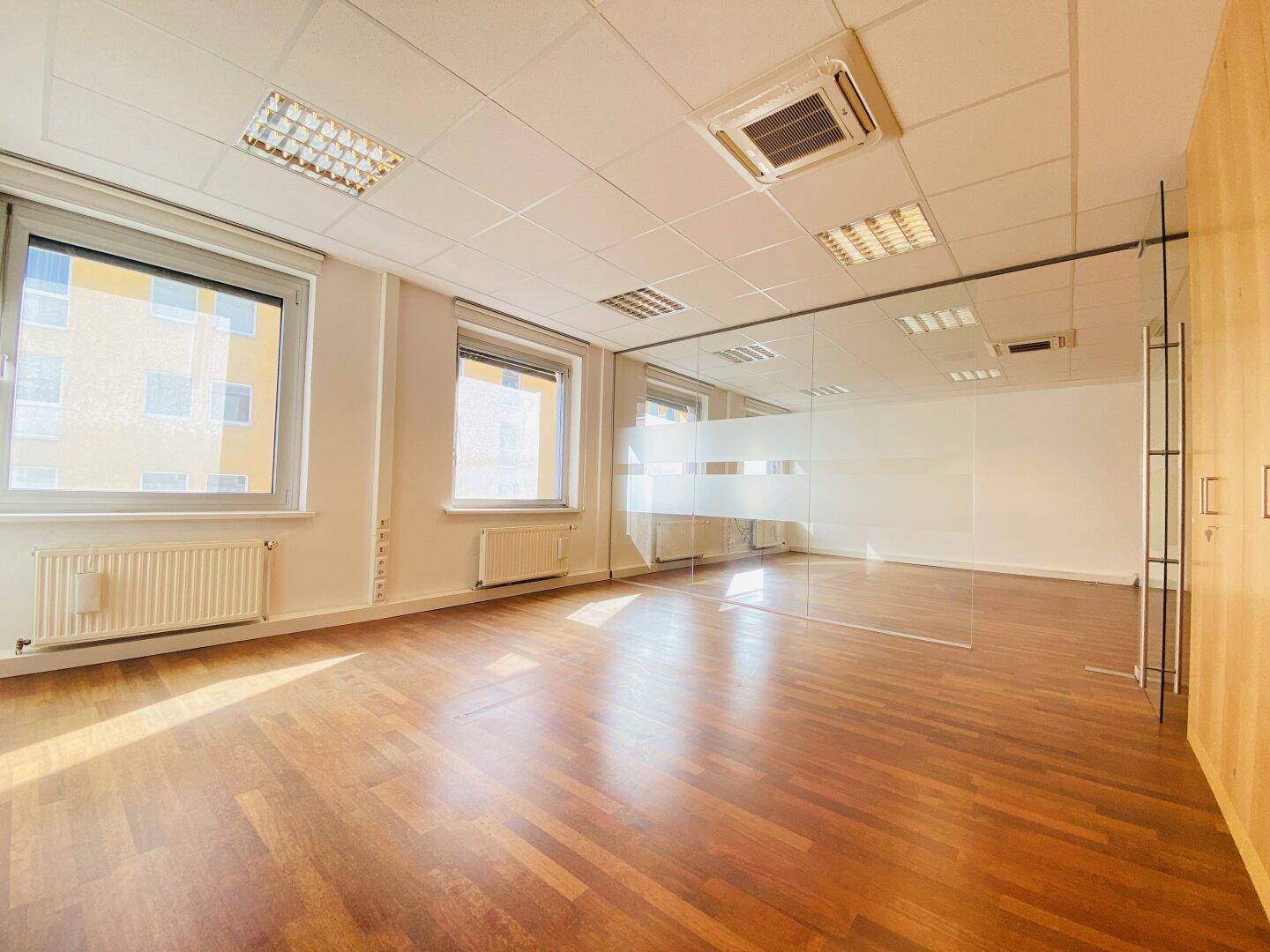 Geräumiges Büro mit Holzboden, großen Fenstern und Glasabtrennung, bietet viel Tageslicht und Flexibilität.