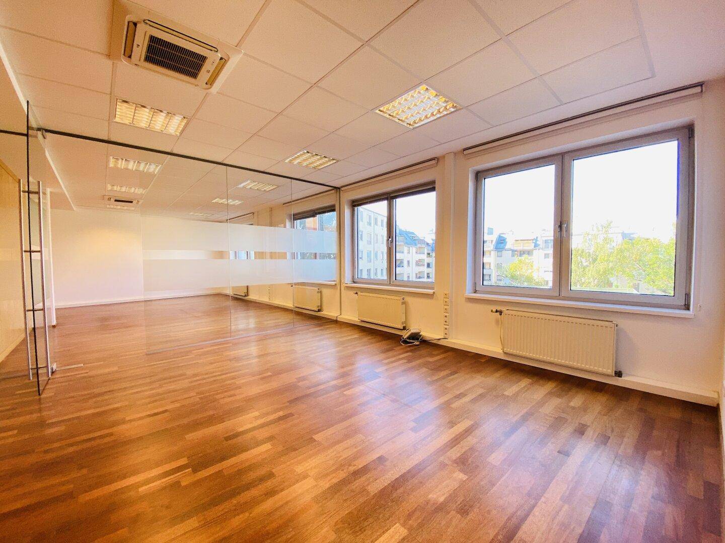 Helles Büro mit Holzboden, großen Fenstern und Klimaanlage, bietet einen weiten Blick über die Stadt.