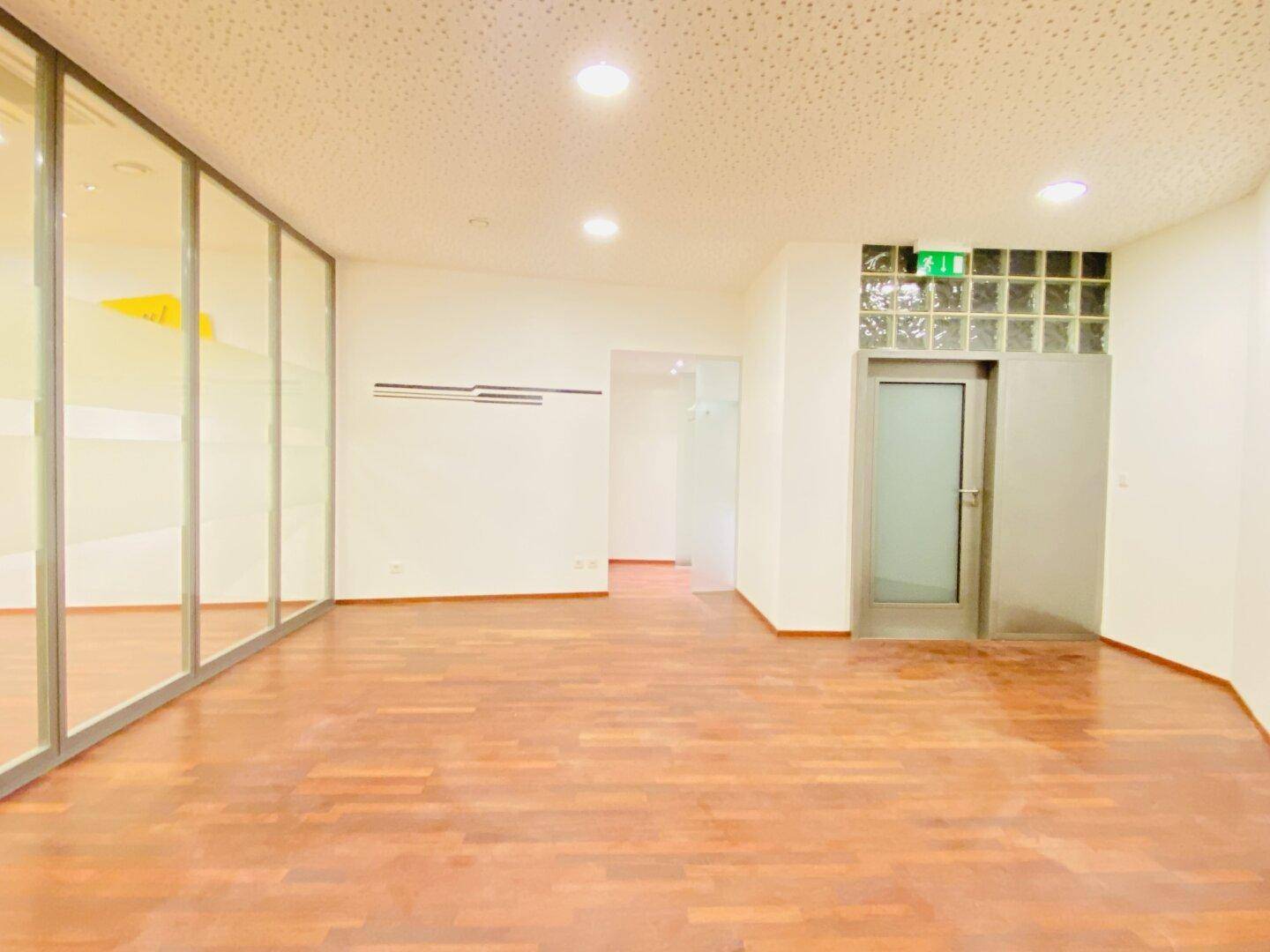Leerer Büroraum mit Holzboden, Glasbausteinen und Deckenbeleuchtung, bereit zur individuellen Gestaltung.