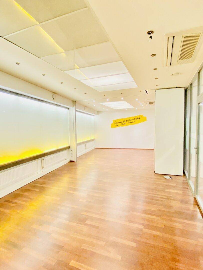 Moderner Büroraum mit Holzboden, indirekter Beleuchtung und gelber Wanddekoration, schafft eine angenehme Arbeitsatmosphäre.